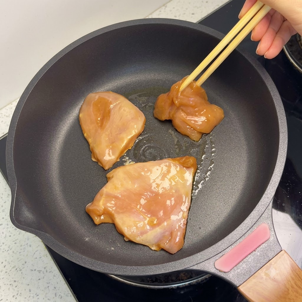 Trozos de pechuga de pollo dorándose en una sartén.