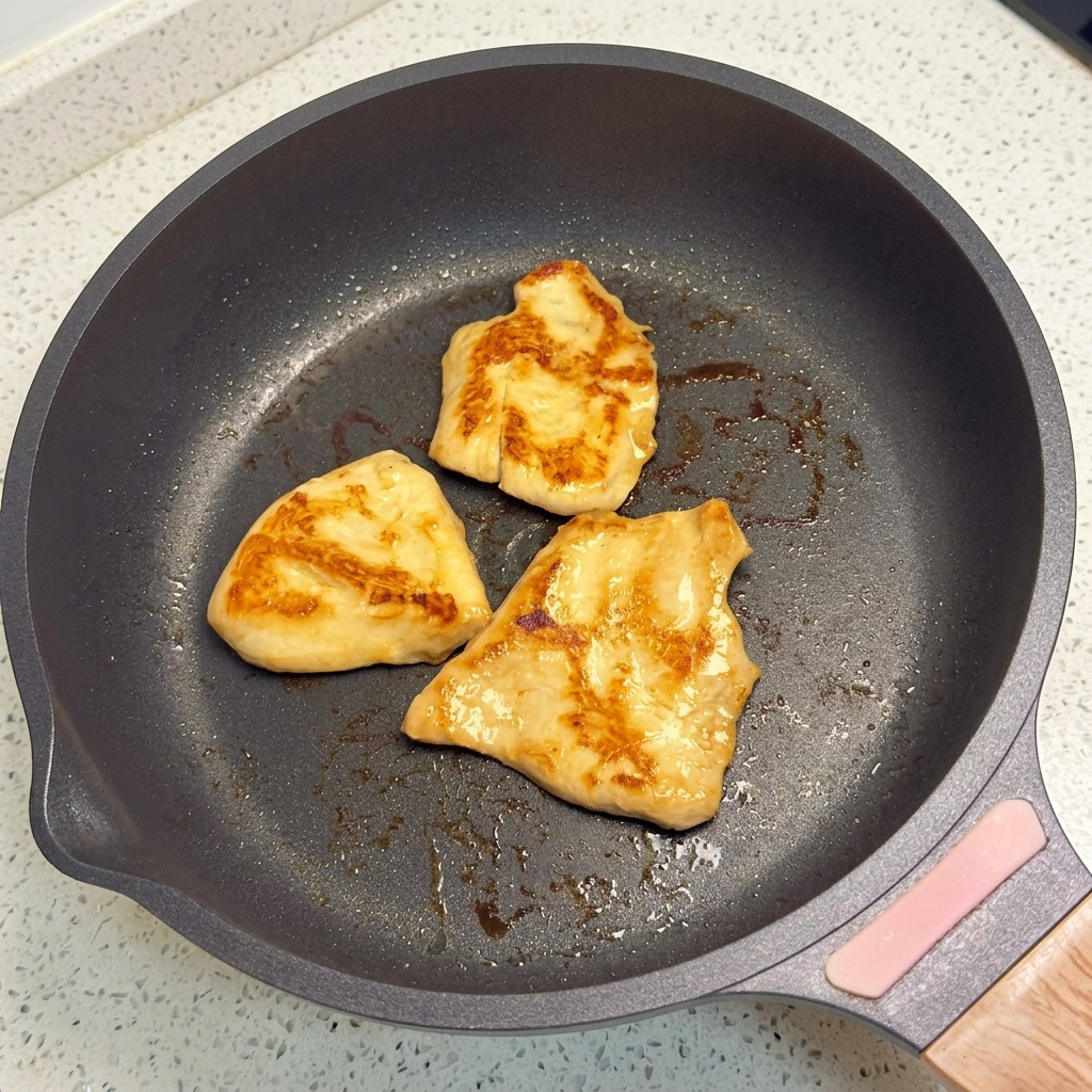 Trozos de pollo friéndose en una sartén plana hasta dorarse.