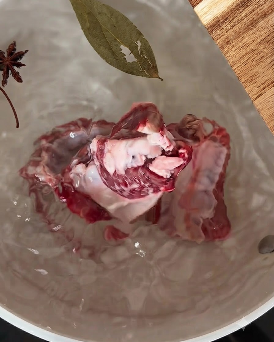 Costillas de cerdo hirviendo a fuego lento en una olla con anís estrellado y una hoja de laurel flotando encima.