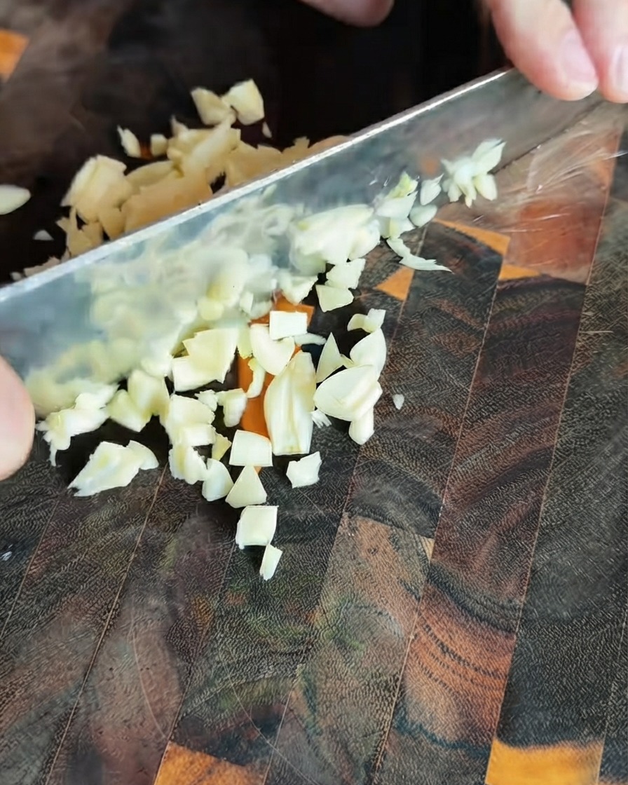 Trozo de ajo fresco picado esparcido sobre una tabla de cortar de madera oscura.