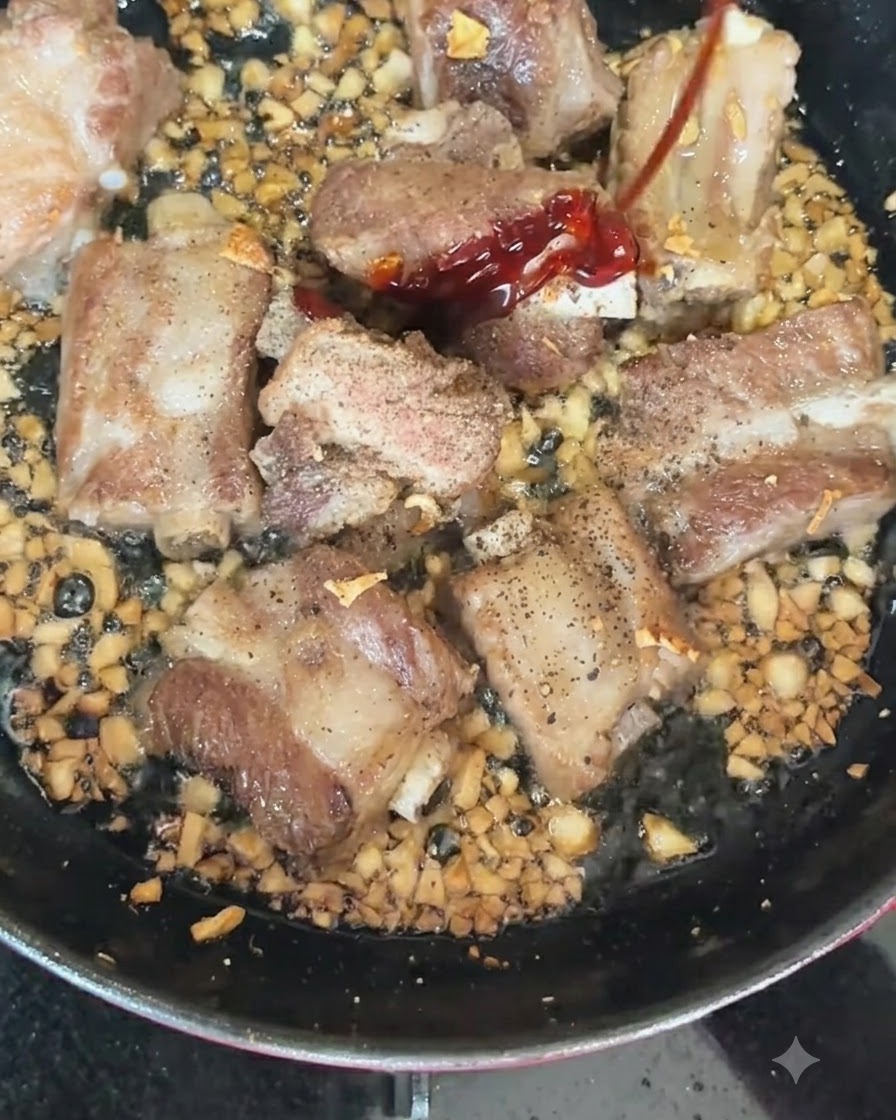 Chiles rojos y verdes siendo añadidos a una sartén caliente que contiene costillas de cerdo dorándose y ajo picado.