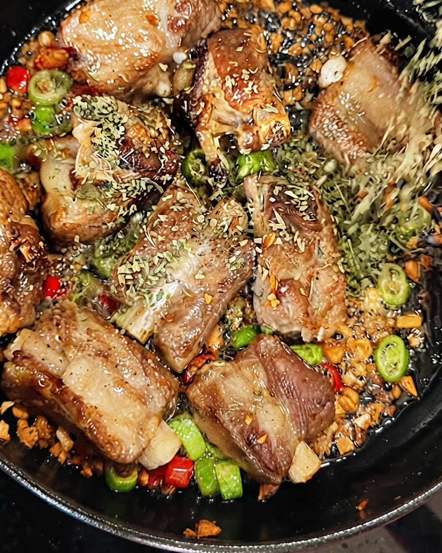 Perejil seco siendo espolvoreado sobre las costillas de cerdo mientras se vierte vino blanco seco en la sartén chisporroteante.
