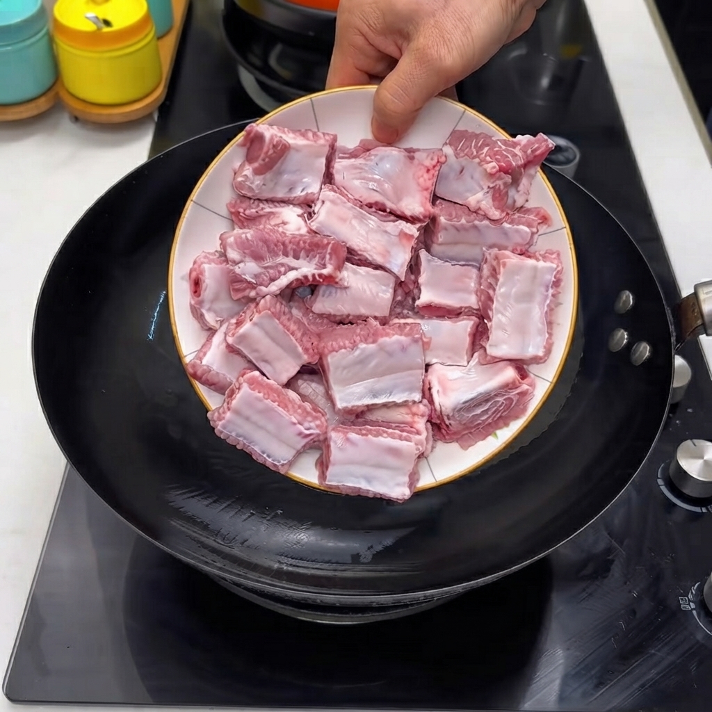 Costillas de cerdo crudas siendo vertidas desde un plato blanco en un wok negro caliente.