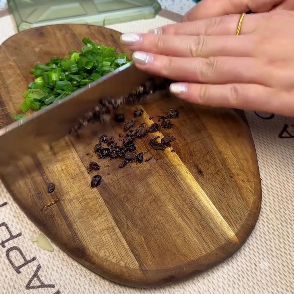 Frijoles negros fermentados y cebollas verdes picadas siendo cortados en una tabla de cortar de madera con un cuchillo.