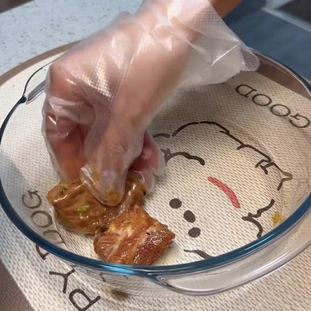 Costillas de cerdo marinadas siendo dispuestas en una capa plana única dentro de un plato para hornear de vidrio transparente.