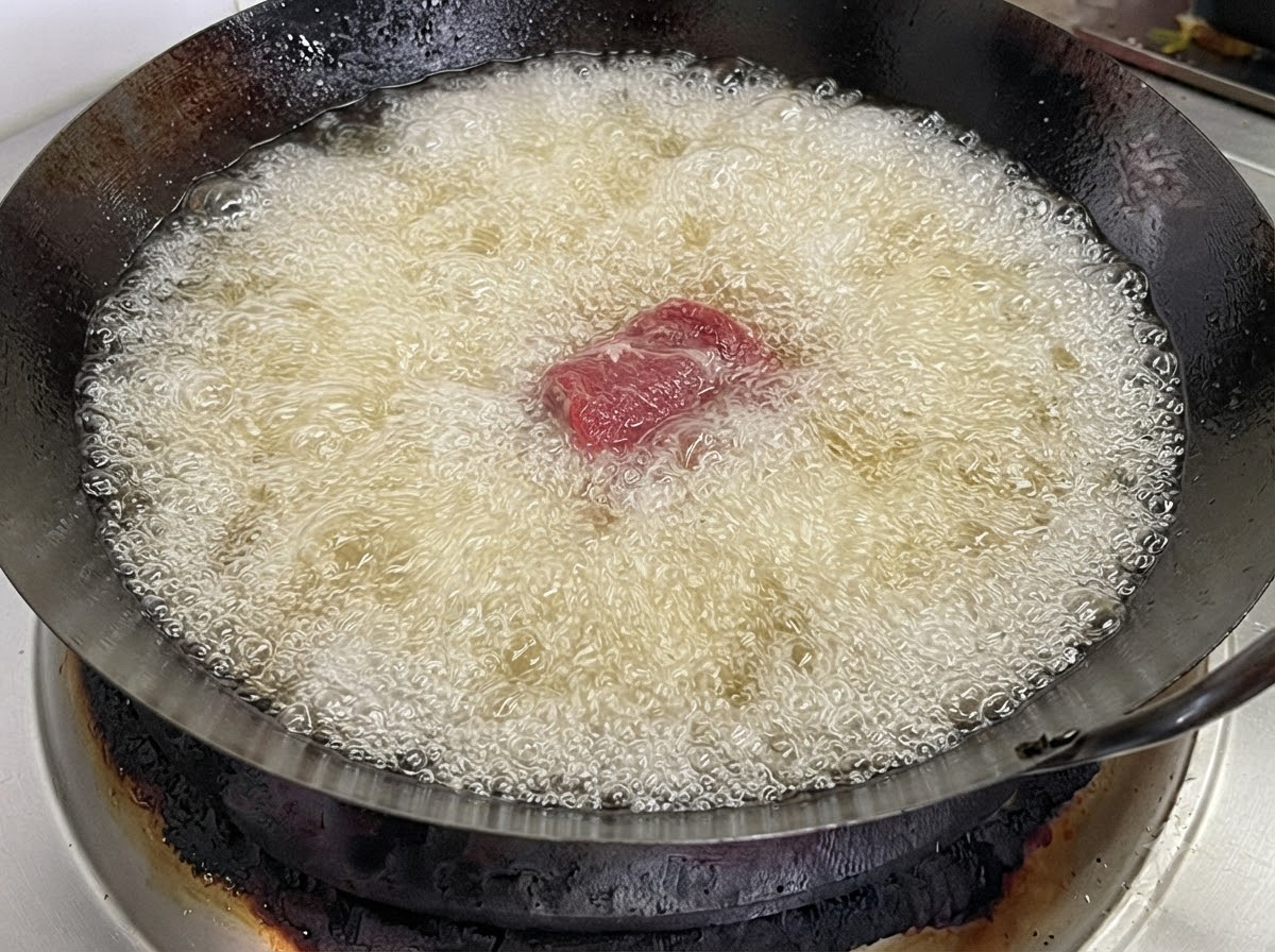 Una sola pieza de costilla de cerdo arrojada a un wok lleno de aceite para freír hirviendo y burbujeante.