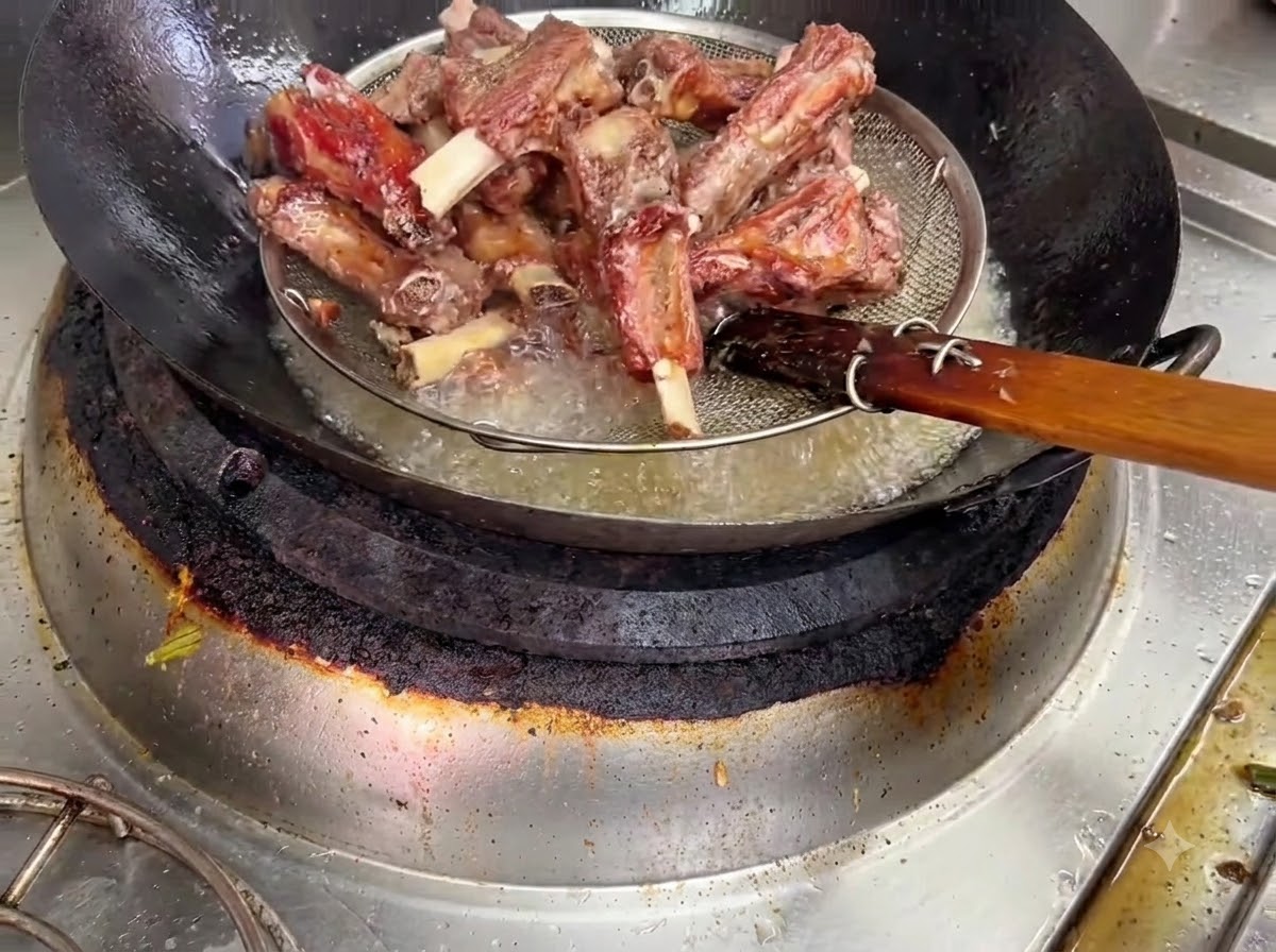 Costillas de cerdo fritas siendo levantadas del aceite caliente en una cesta coladora de alambre.