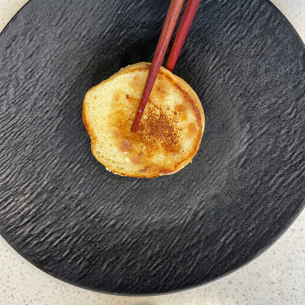 La mitad inferior de un pan de hamburguesa tostado descansando sobre un plato negro con textura.