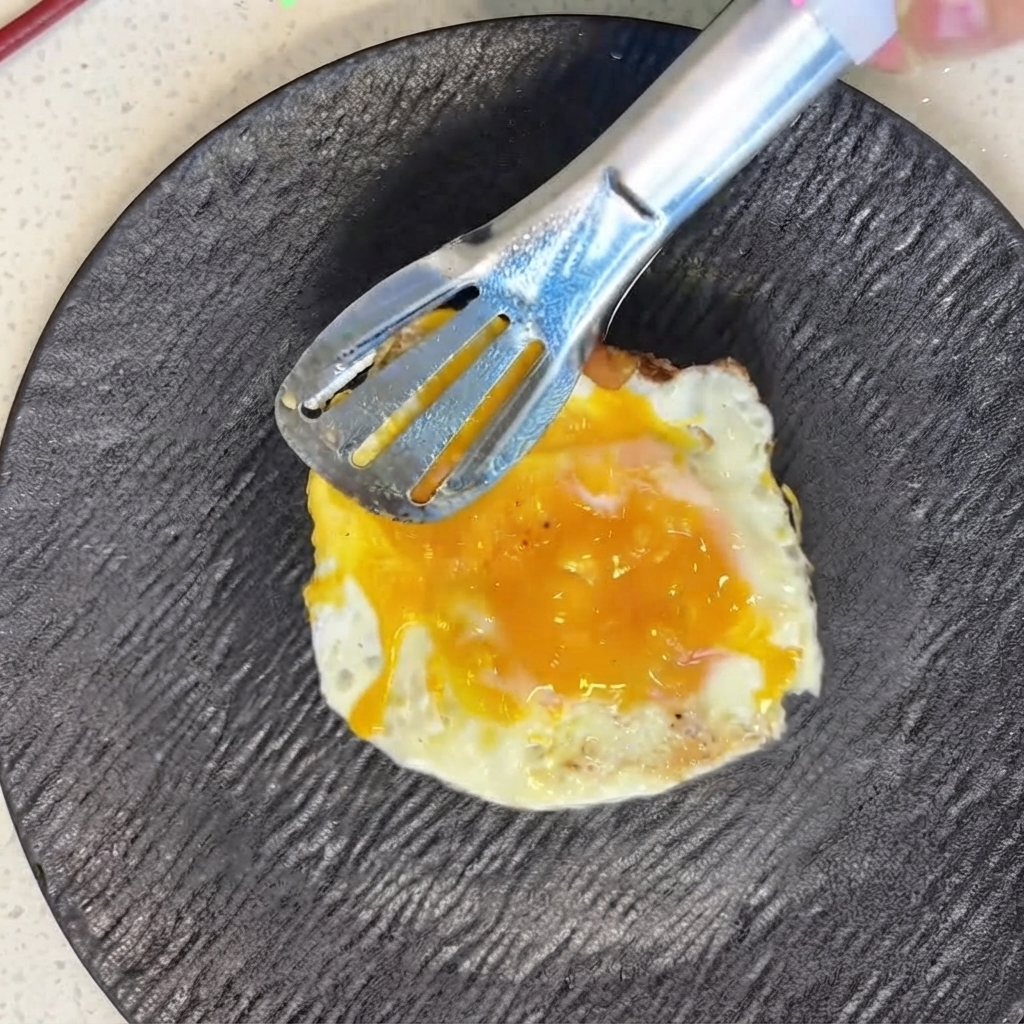 Un huevo recién frito siendo colocado cuidadosamente sobre rodajas de tomate con unas pinzas de metal.