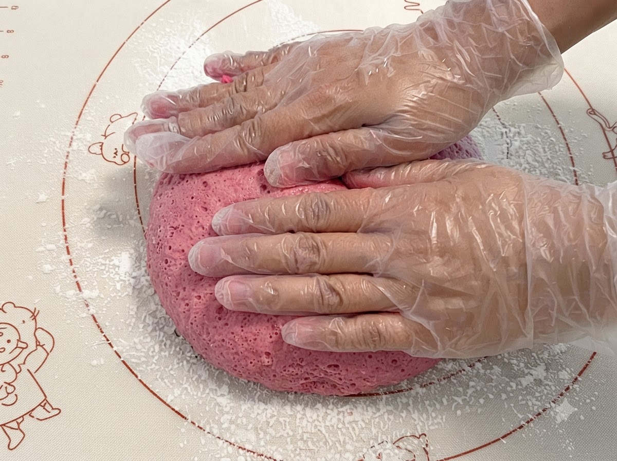 Masa rosada fermentada siendo presionada y amasada sobre una estera de silicona.