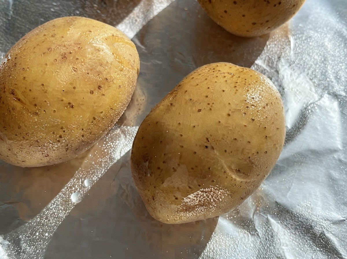 Papas crudas enteras untadas con aceite sobre una hoja de papel aluminio.