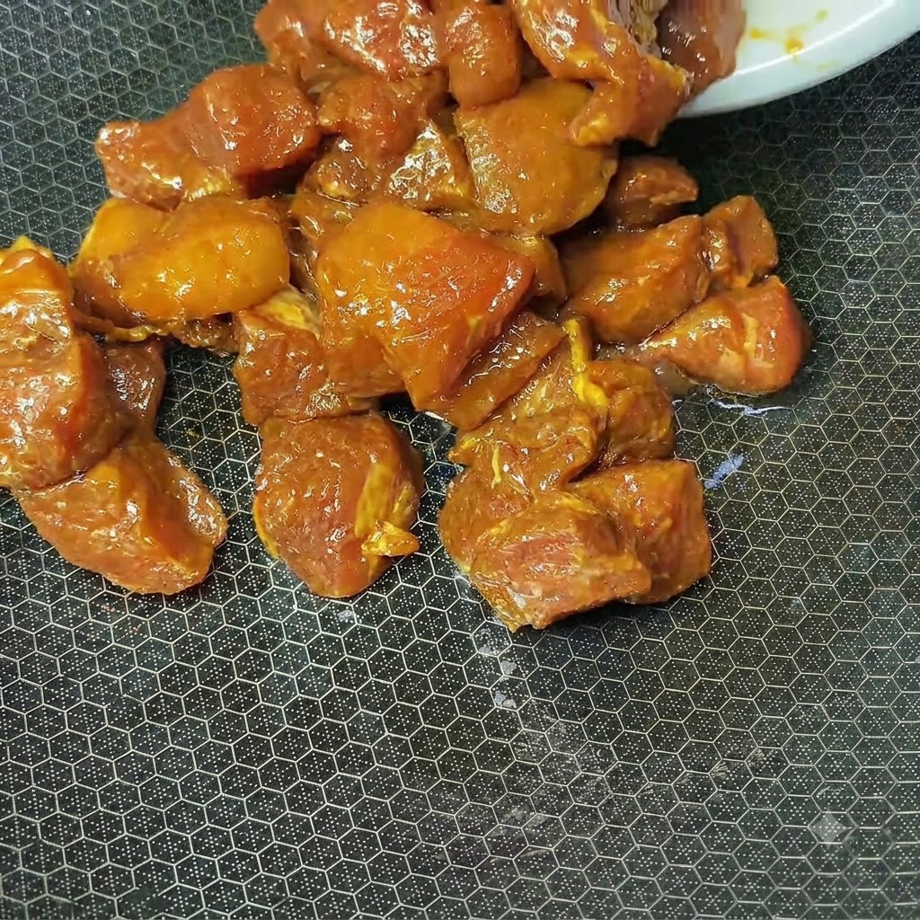 Cubos de cerdo marinados de color marrón rojizo cocinándose en un wok caliente texturizado.