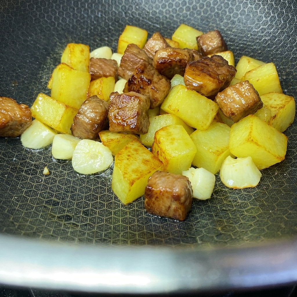 Cubos de patata dorados y crujientes y cubos de cerdo sellados combinados en un wok.