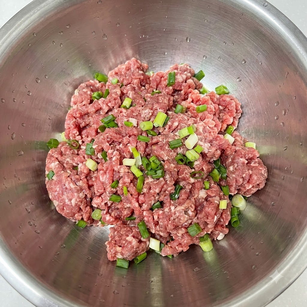 Cebolla verde recién picada colocada sobre carne picada en un bol de acero inoxidable.