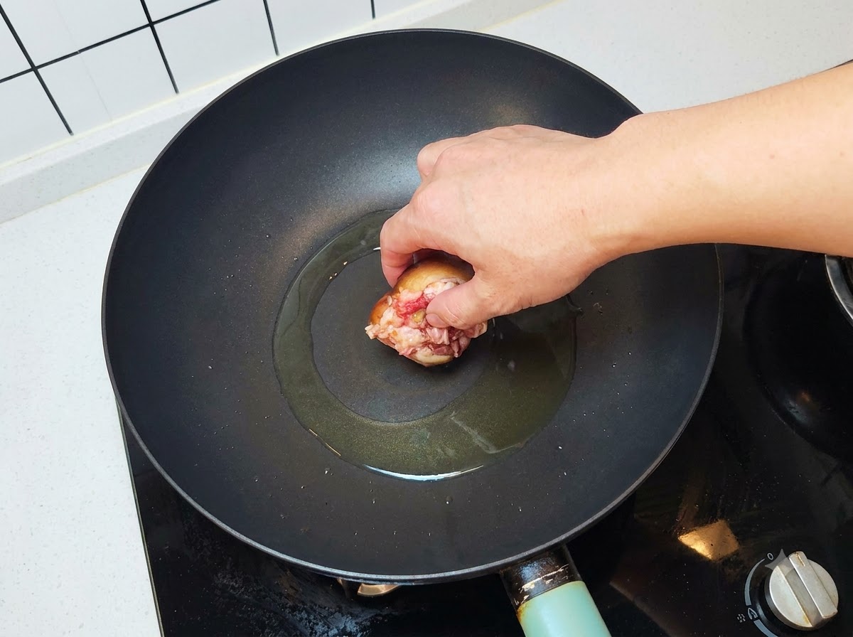 Una seta rellena colocándose con el lado de la carne hacia abajo en un wok caliente con aceite.
