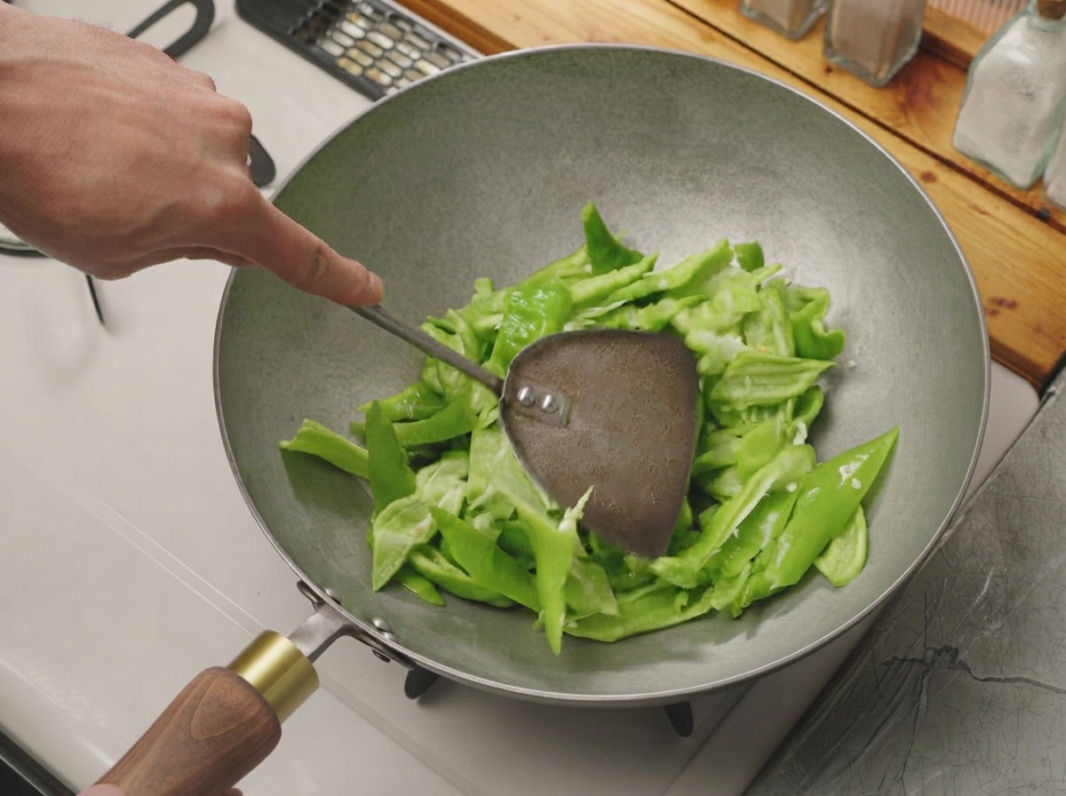 Pimientos verdes cortados siendo salteados con una espátula de metal en un wok caliente y seco.