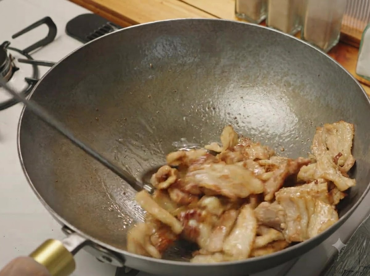 Rodajas de panceta de cerdo siendo salteadas en un wok hasta que estén ligeramente doradas y crujientes.