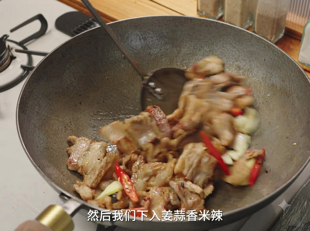 Jengibre, ajo y chiles rojos siendo mezclados con los trozos de cerdo dorado en un wok.
