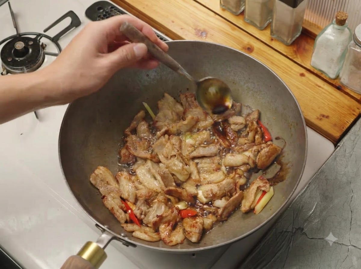 Salsa de soja siendo vertida desde una cuchara sobre el borde caliente de un wok que contiene carne y aromáticos.