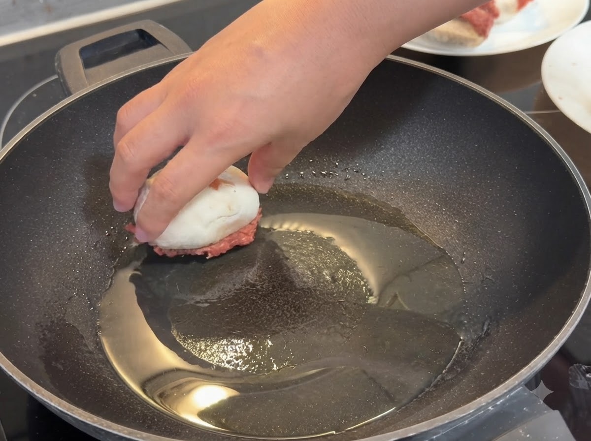 Una mano coloca un champiñón relleno con la parte de la carne hacia abajo en una sartén caliente untada con aceite.