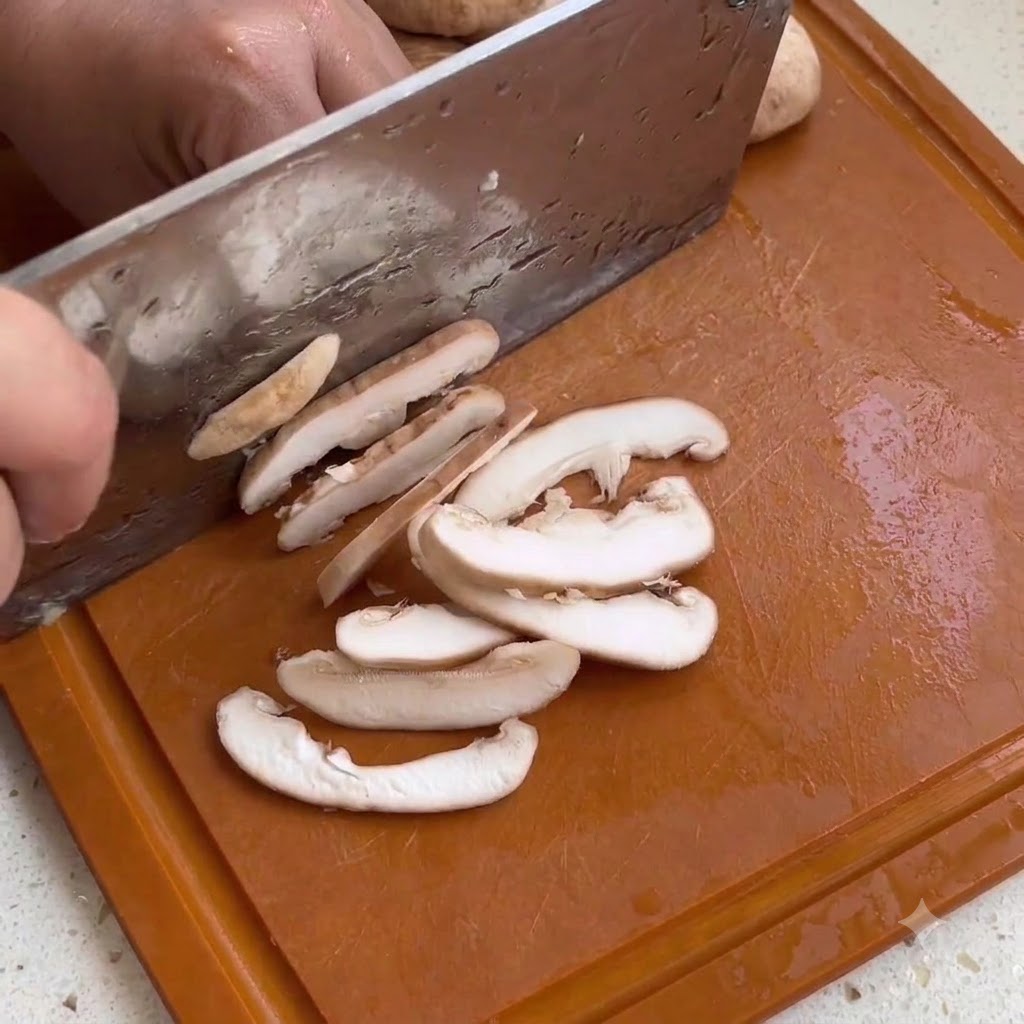 Rebanadas de champiñón shiitake siendo cortadas en una tabla de cortar de madera con un cuchillo de cocina.