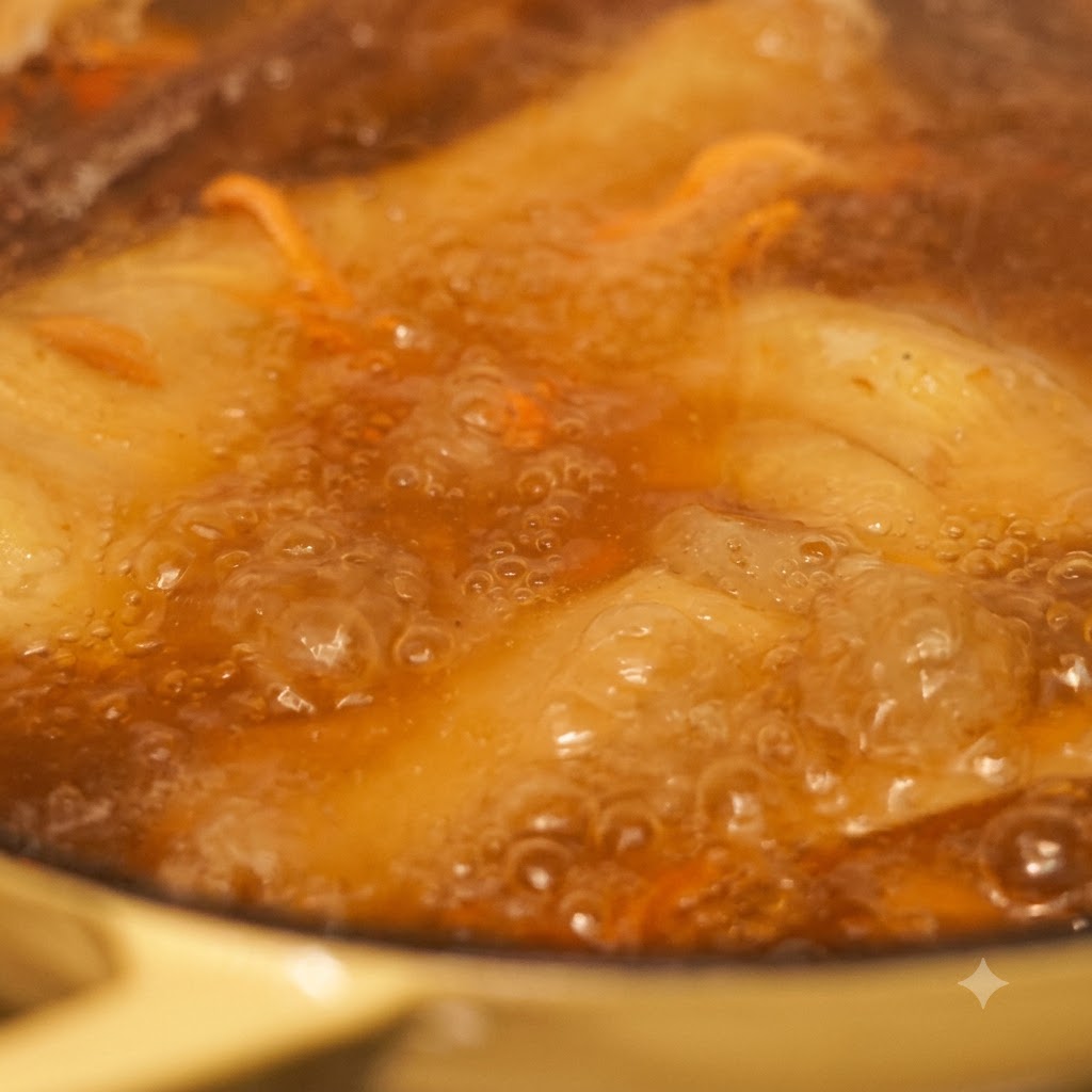 Primer plano de fideos y verduras cociéndose en un caldo burbujeante.