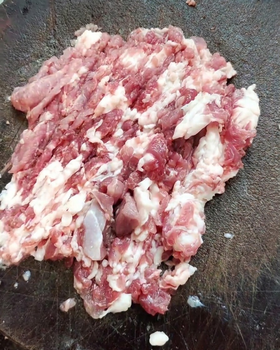 Un cuchillo de carnicero afilado descansando sobre un montón de carne de hombro de cerdo recién picada en una tabla de madera texturizada.