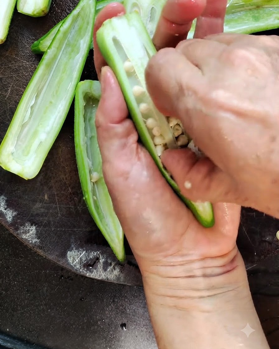 Un cuchillo de cocina cortando por la mitad una vaina de okra verde fresca en una tabla de madera.