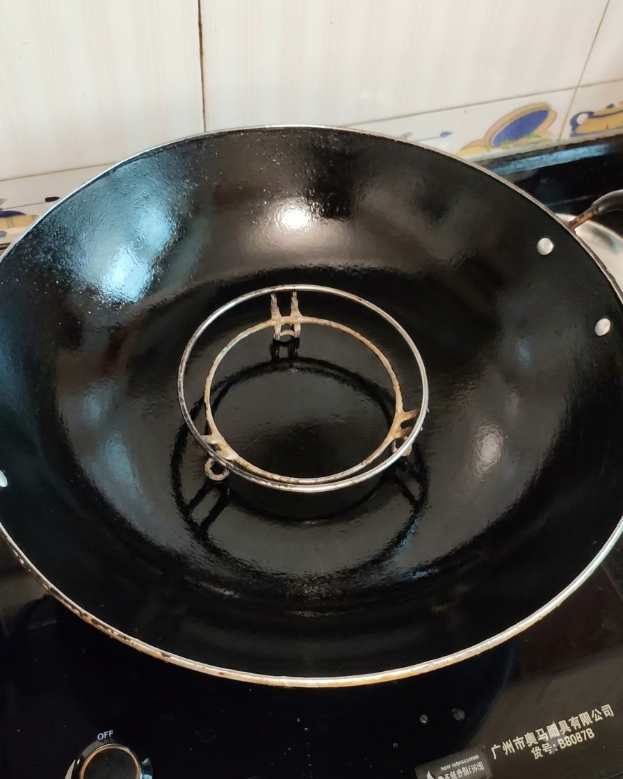 Una rejilla de vapor vacía colocada dentro de un wok negro grande listo para cocinar.