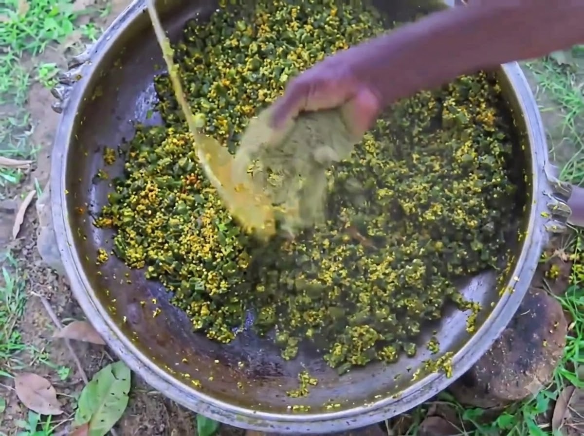 La mano de una persona mezclando pimienta negra en polvo en una olla de hierro grande llena de okra y huevos en cocción.