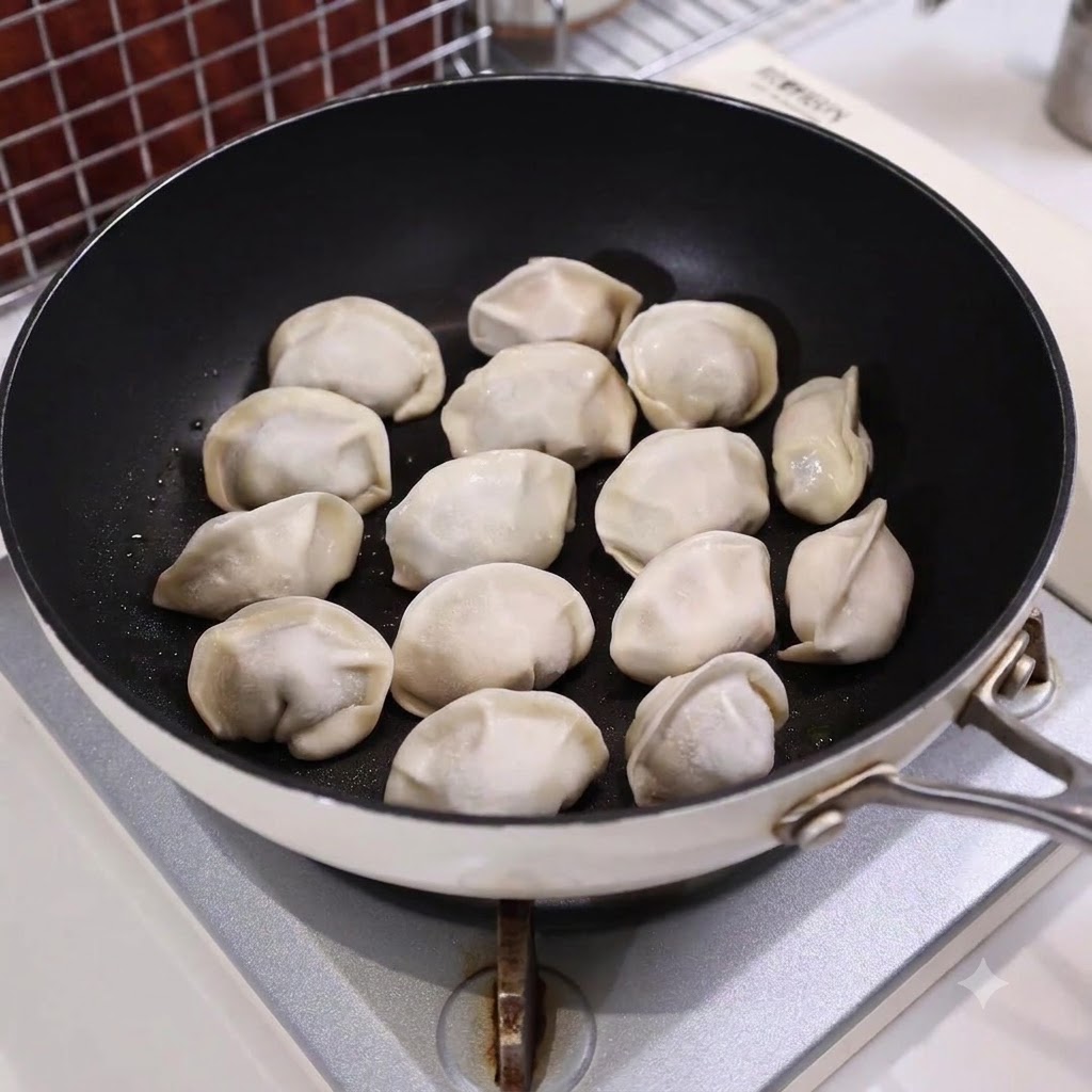 Una sartén llena de empanadillas dispuestas parcialmente sumergidas en agua en una estufa.