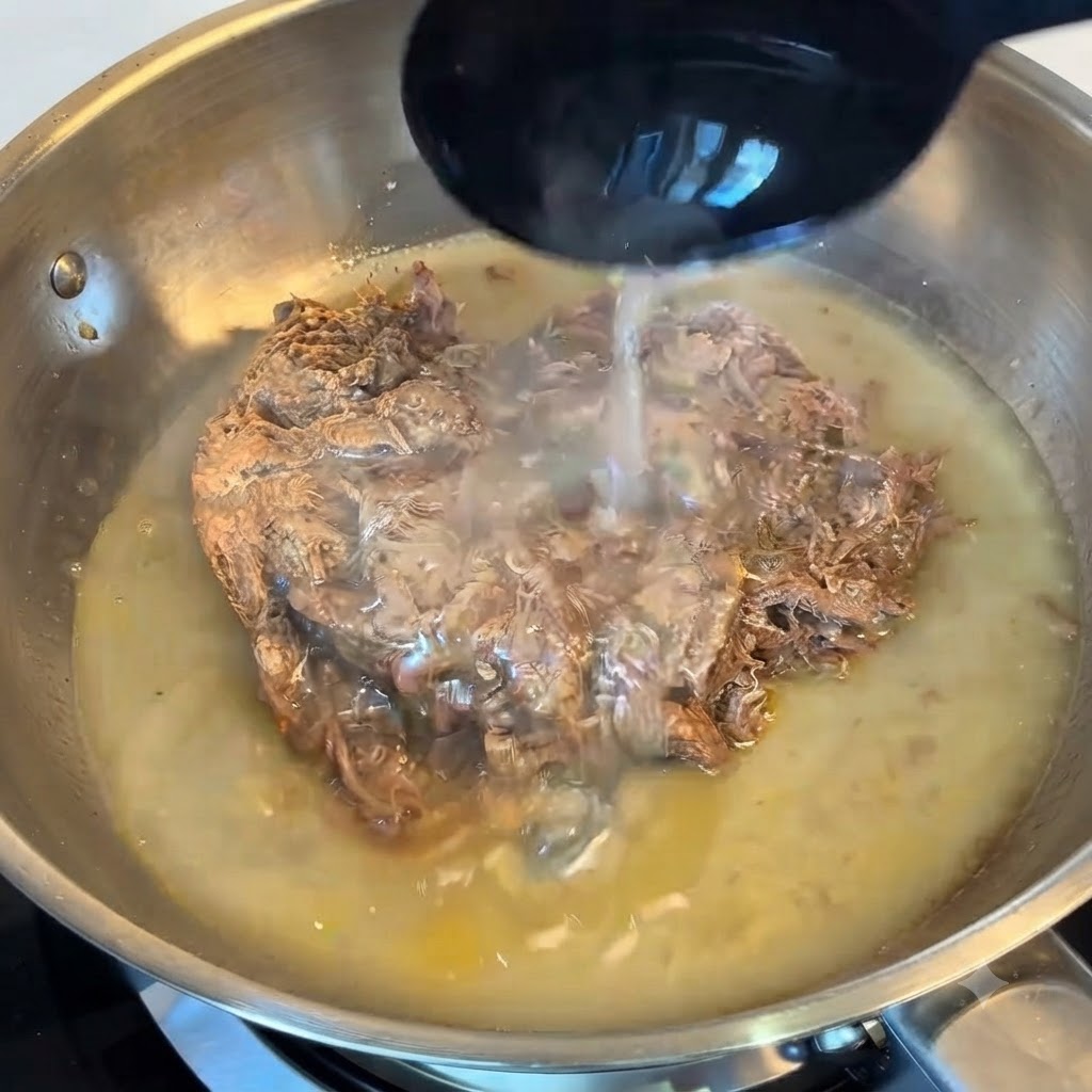 Un cucharón vertiendo agua rica en almidón sobre la carne en una sartén de acero inoxidable.