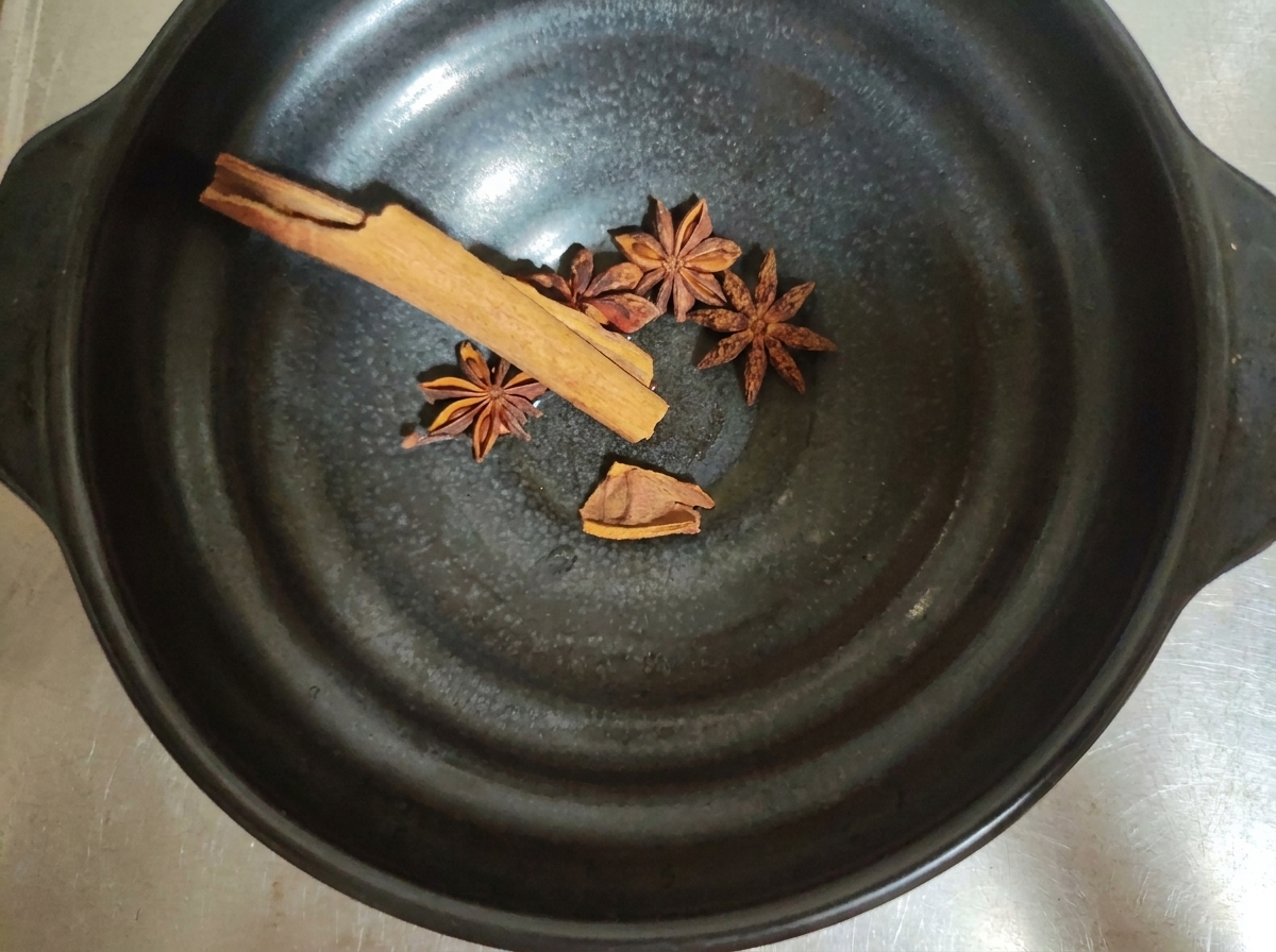 Especias enteras como anís estrellado y canela dentro de un bol oscuro.