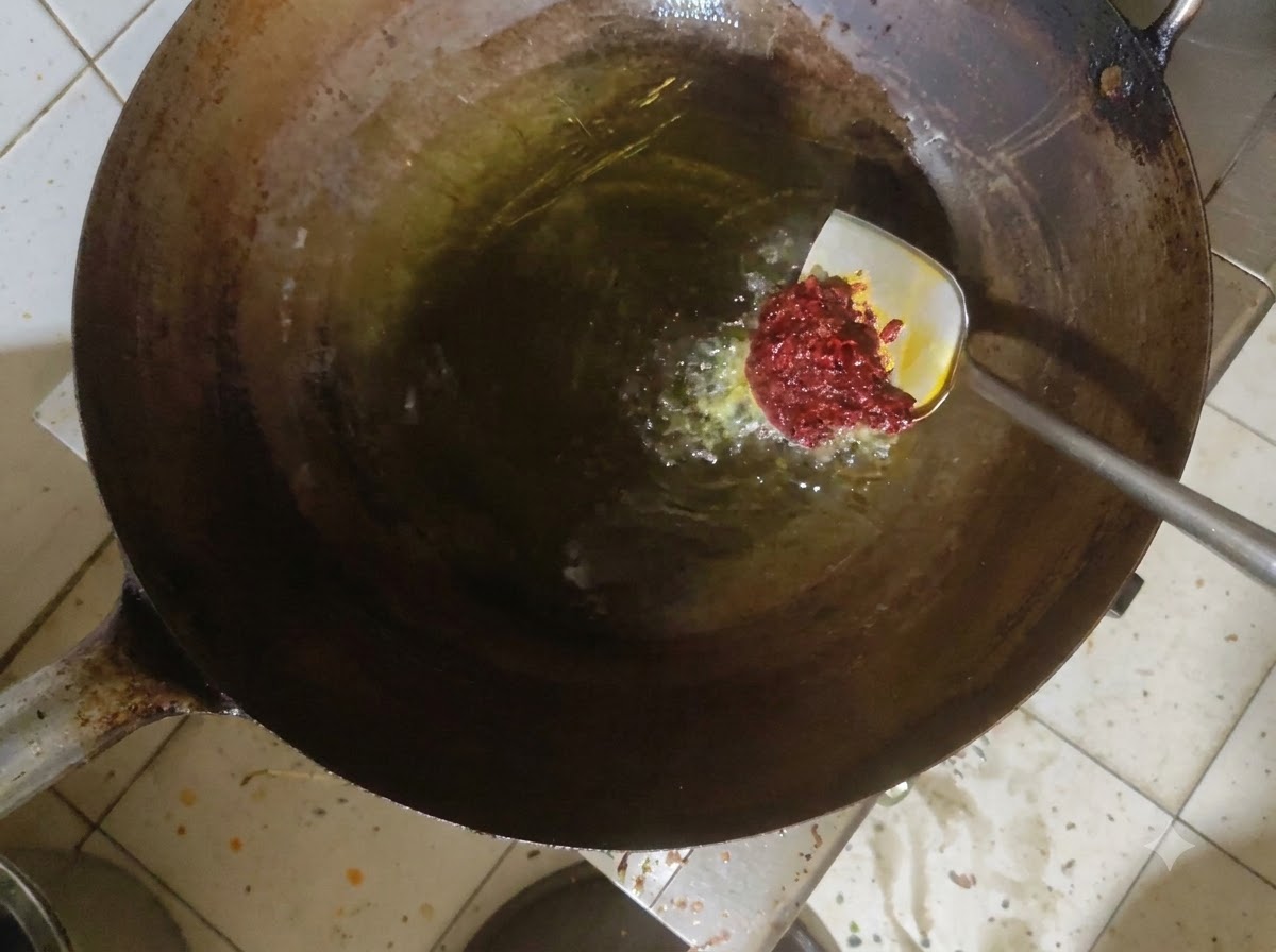 Pasta doubanjiang siendo revuelta en aceite caliente dentro de un wok.