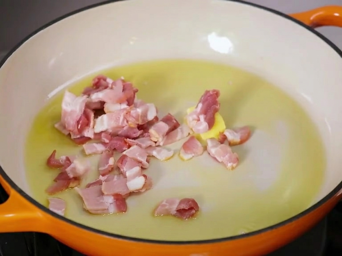 Trozos de tocino chisporroteando en una sartén con mantequilla derretida y aceite de oliva.