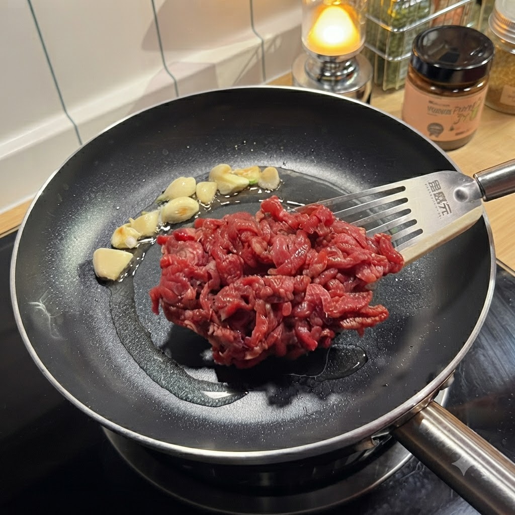 Tiras de carne cruda sazonada colocándose con una espátula en una sartén caliente que contiene ajo salteado.