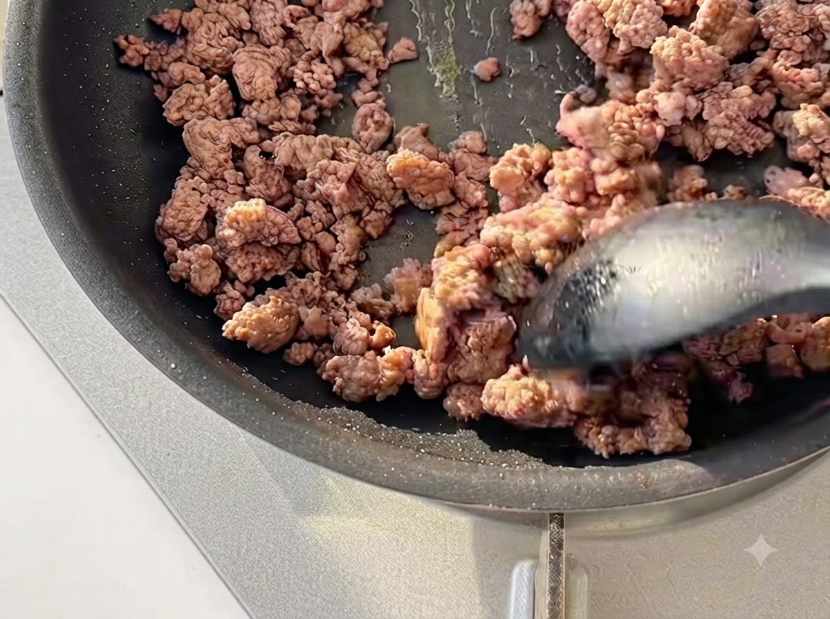 Carne picada siendo salteada con una espátula en una sartén negra hasta que esté ligeramente dorada.