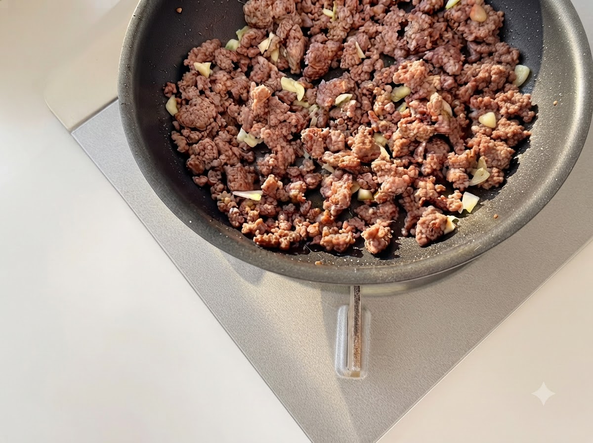 Ajo picado y tomates en dados siendo salteados junto con carne picada dorada en una sartén.