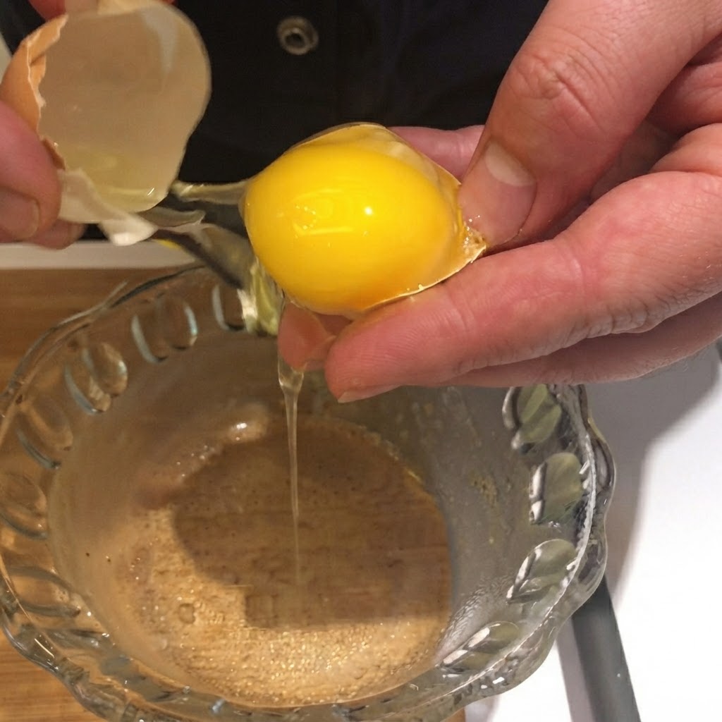 Una yema de huevo siendo separada y cayendo de su cáscara en un tazón de vidrio transparente.