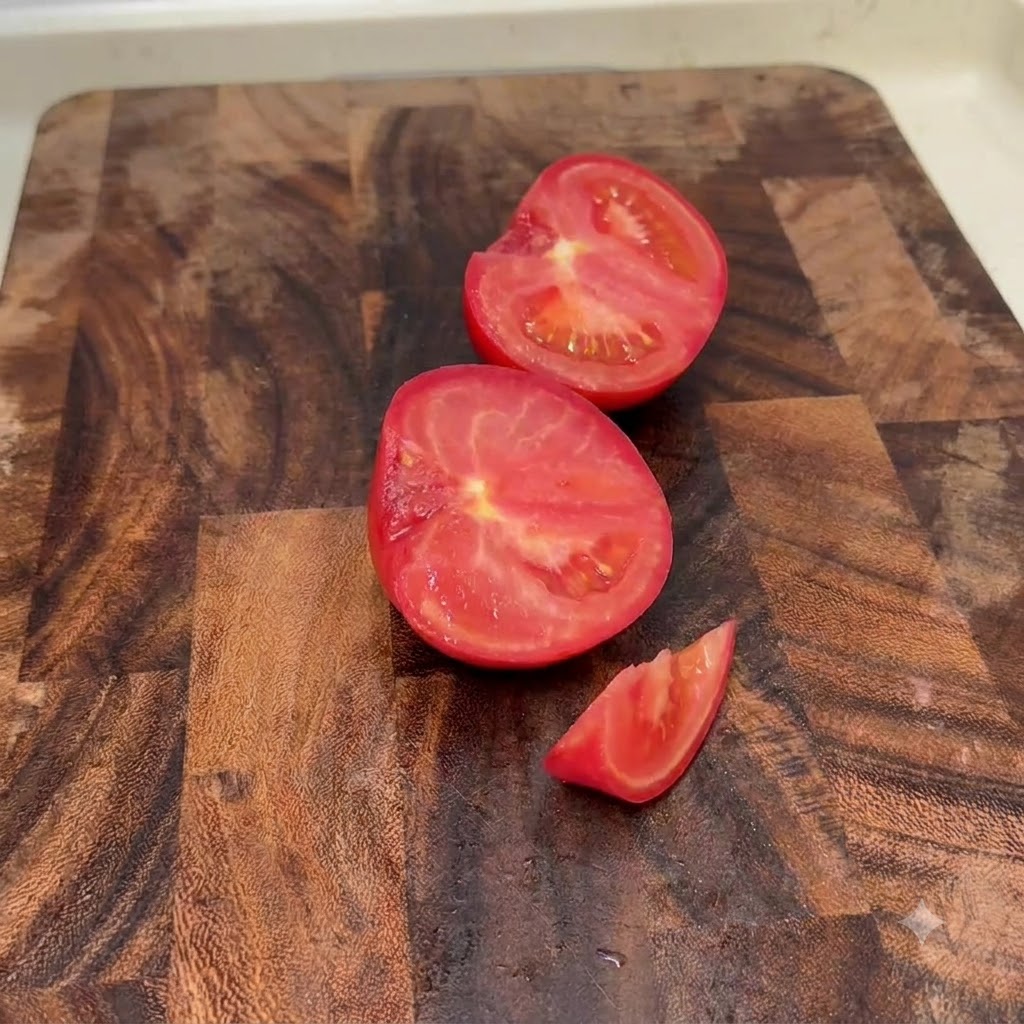 Tomates frescos cortados en mitades y trozos pequeños sobre una tabla de cortar de madera.