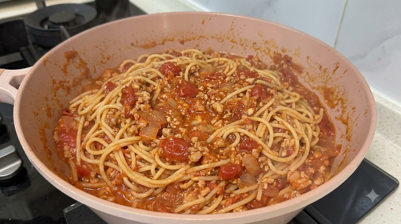 Espaguetis recién cocinados mezclados con una rica y espesa salsa de carne roja boloñesa en una sartén rosa