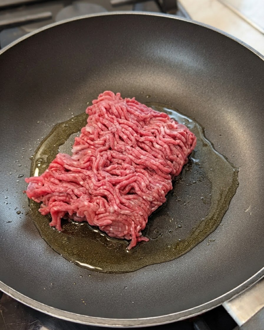 Carne picada cruda en una sartén con aceite, cebolla y ajo.