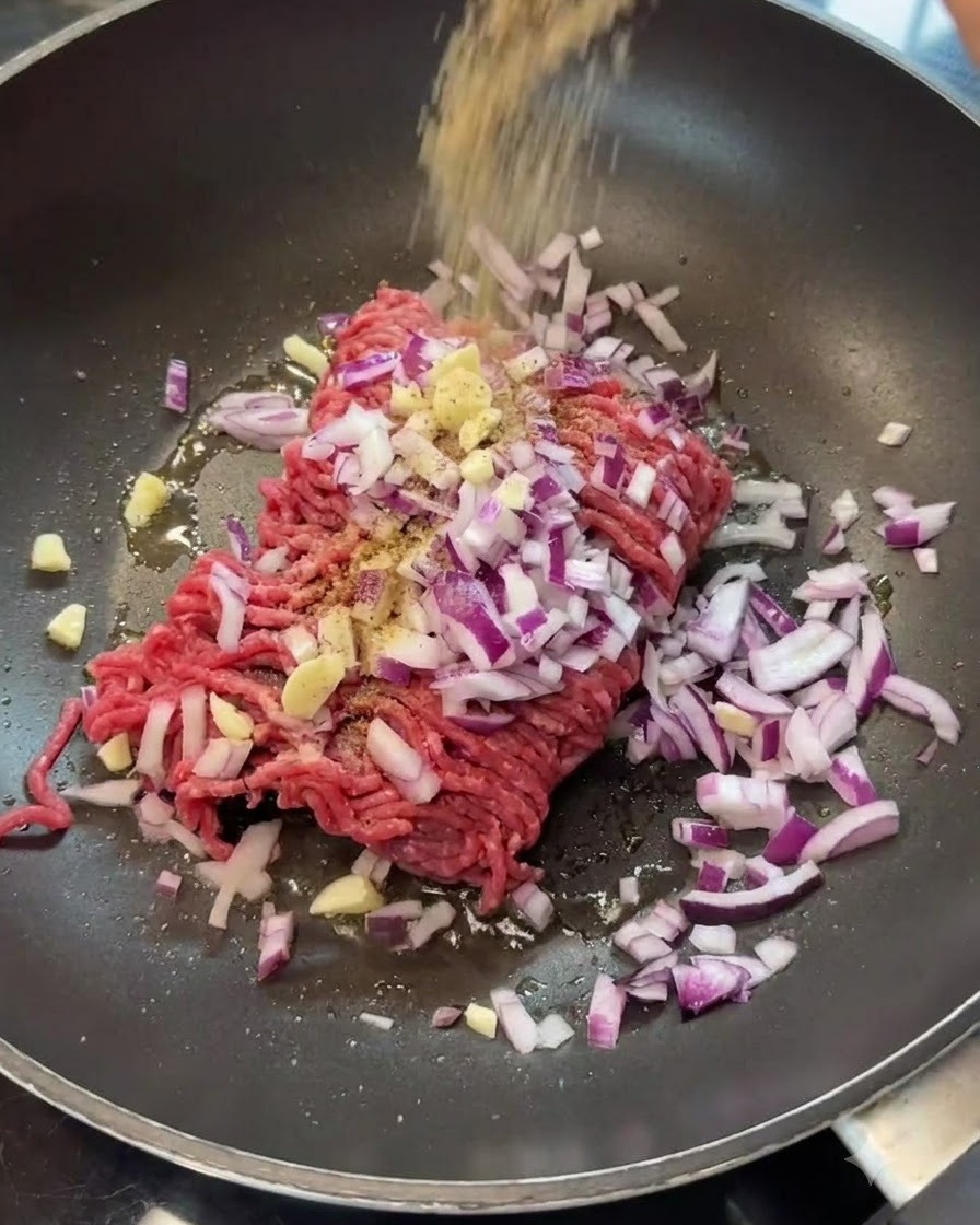 Especias esparciéndose sobre la carne picada y la cebolla en una sartén.