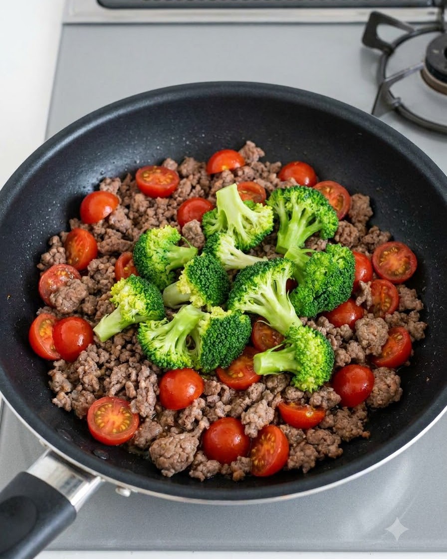 Flores de brócoli verde y tomates cherry rojos brillantes esparcidos sobre la carne picada cocida en una sartén.