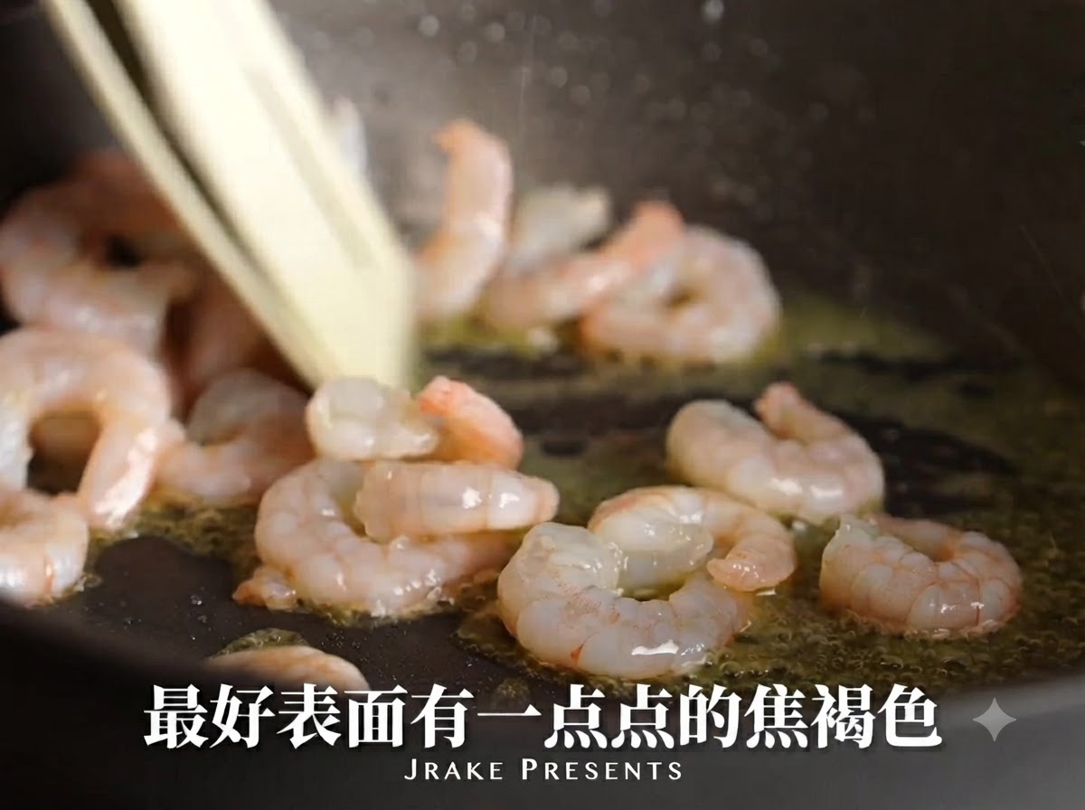 Camarones sellándose en una sartén con aceite, volviéndose rosados y desarrollando una superficie caramelizada.