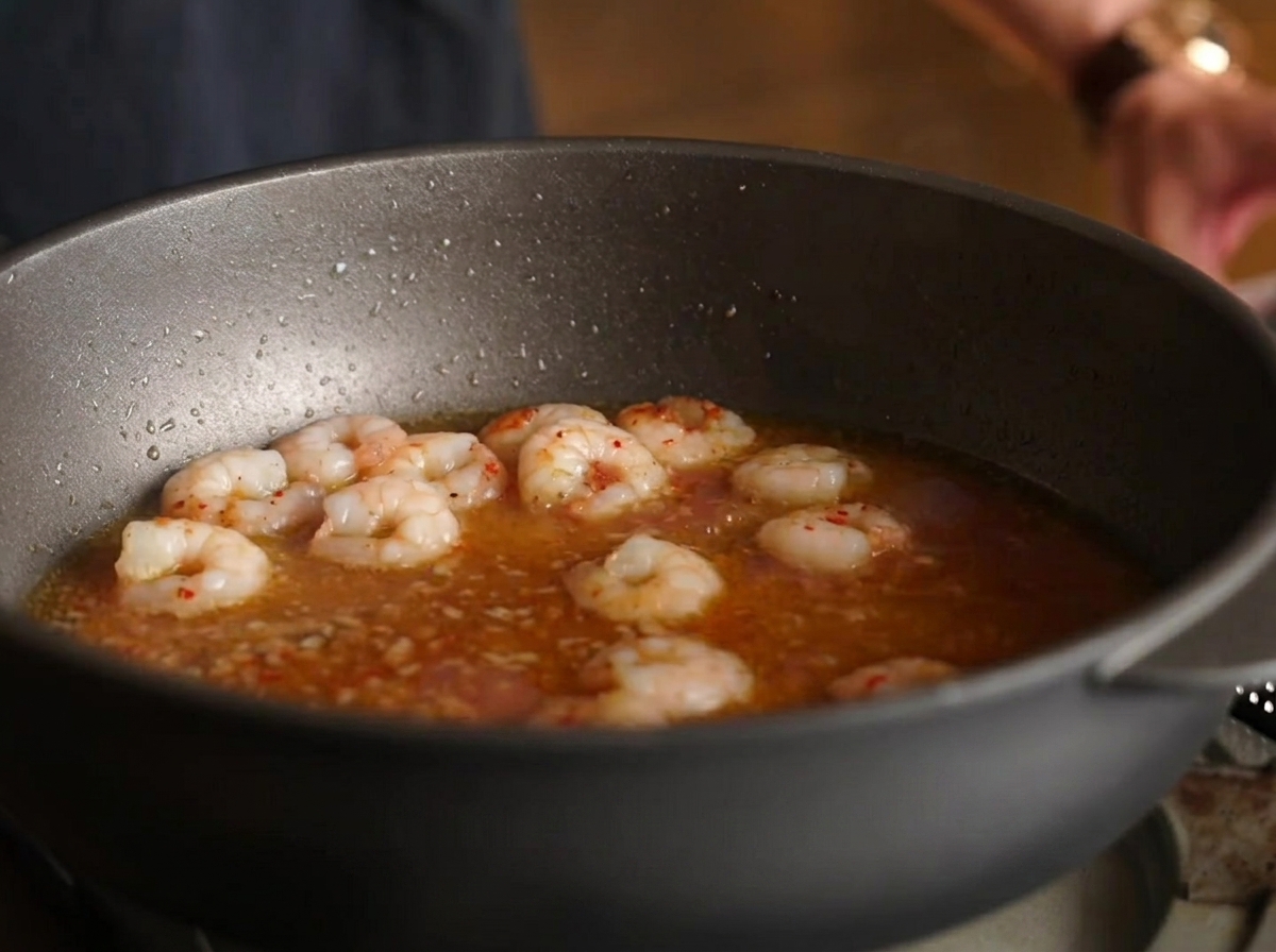 Fideos de espagueti mezclados en la sartén con camarones, caldo y salsa.