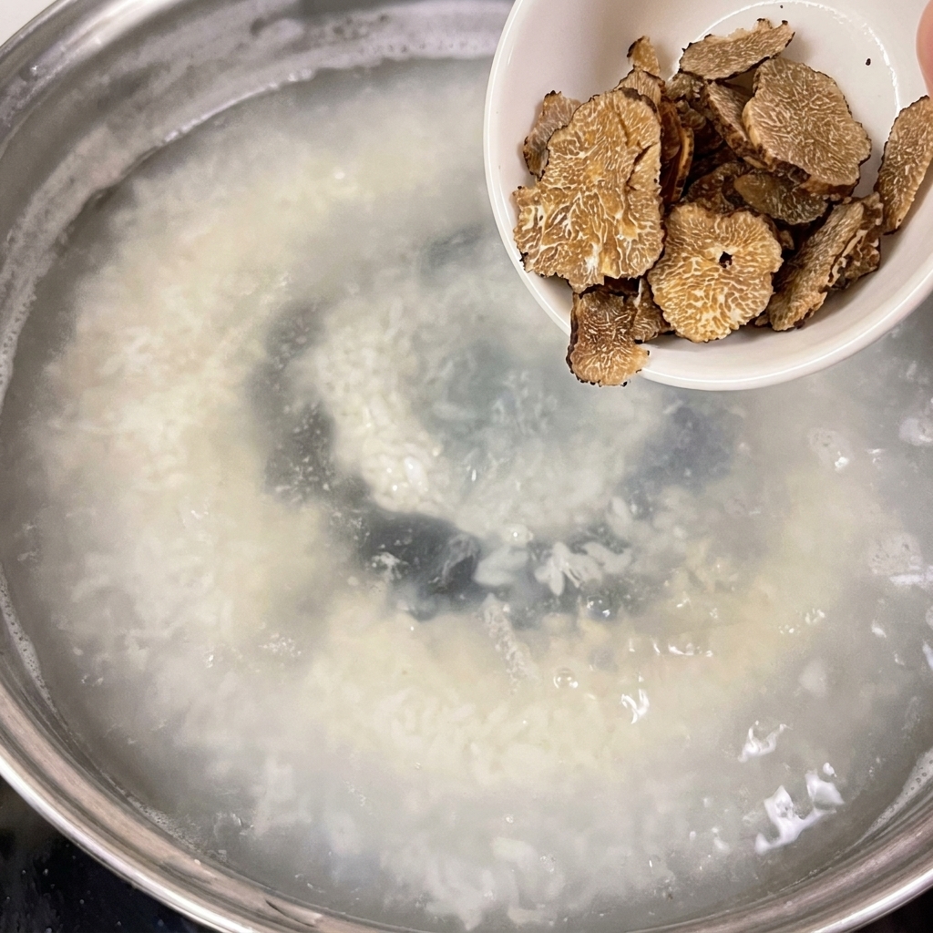 Un pequeño cuenco blanco con trufas en rodajas que se vierten en una olla con agua a fuego lento.