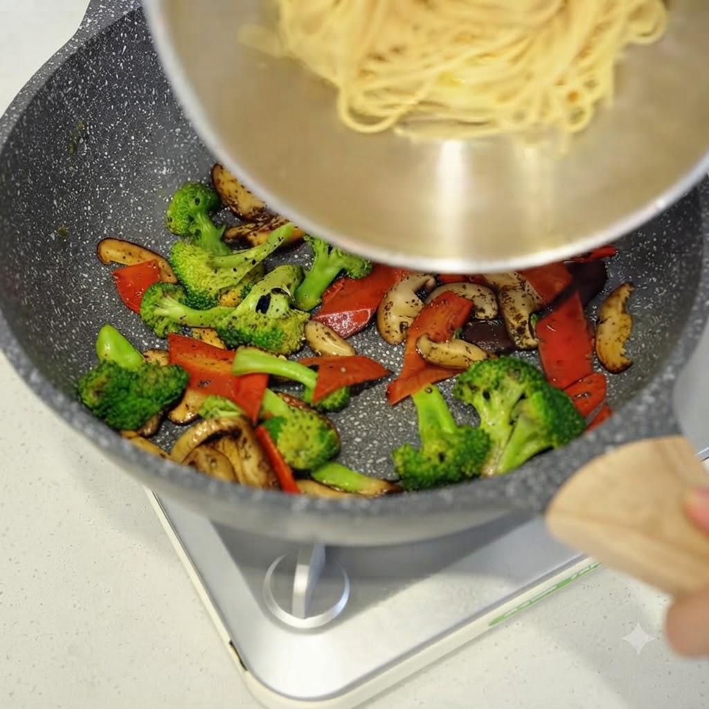 Espaguetis cocidos siendo añadidos desde un tazón a la sartén con verduras salteadas.