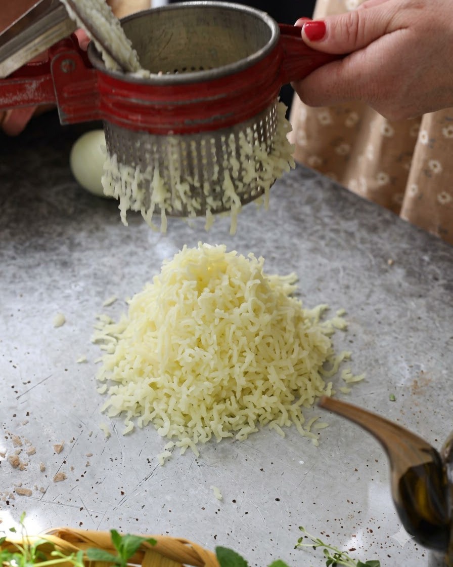 Patatas cocidas calientes siendo pasadas a través de un pasapurés rojo formando una pila esponjosa sobre la mesa.