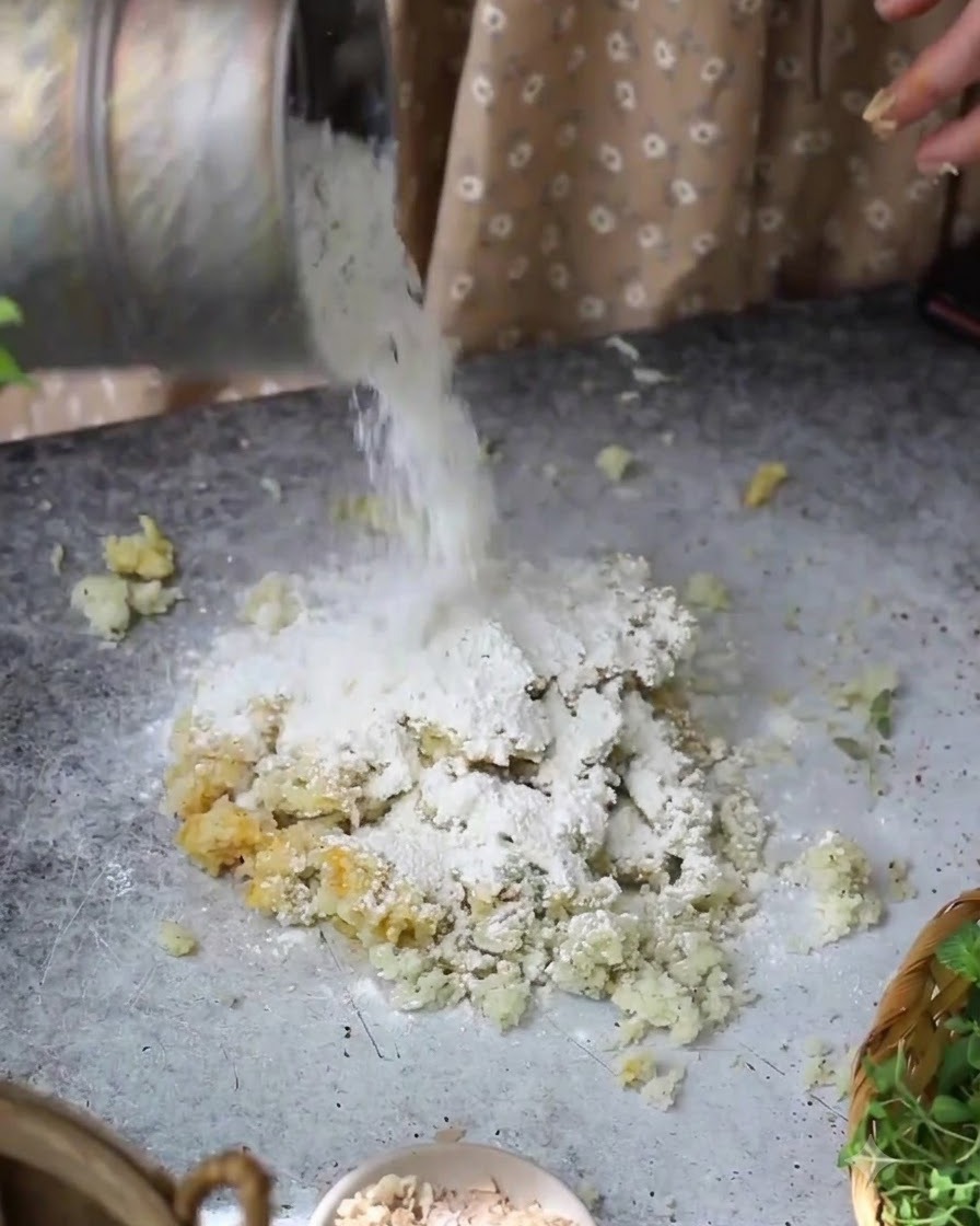 Harina siendo vertida desde un recipiente sobre la mezcla de patata y huevo en la mesa.